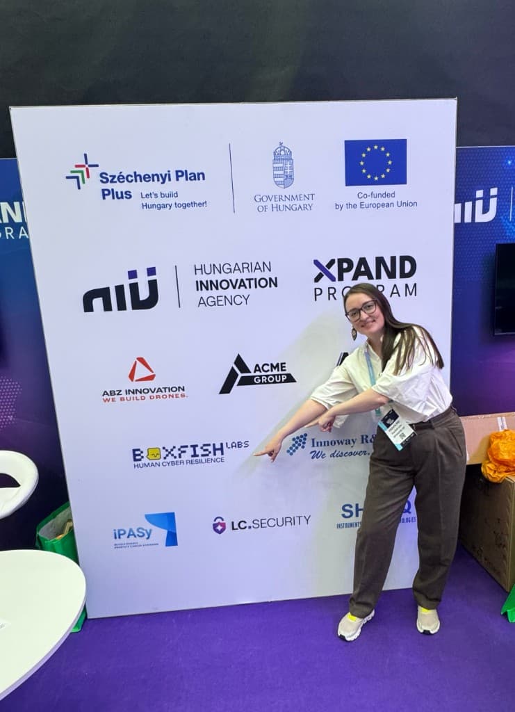 Viktoria Biki pointing to the Boxfish Labs logo at the NIÜ stand